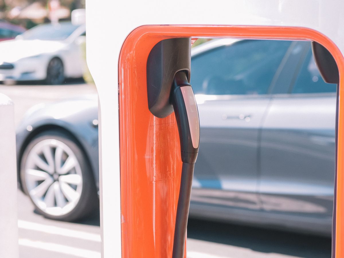 Electric vehicle plugged into a charger with the car parked behind it